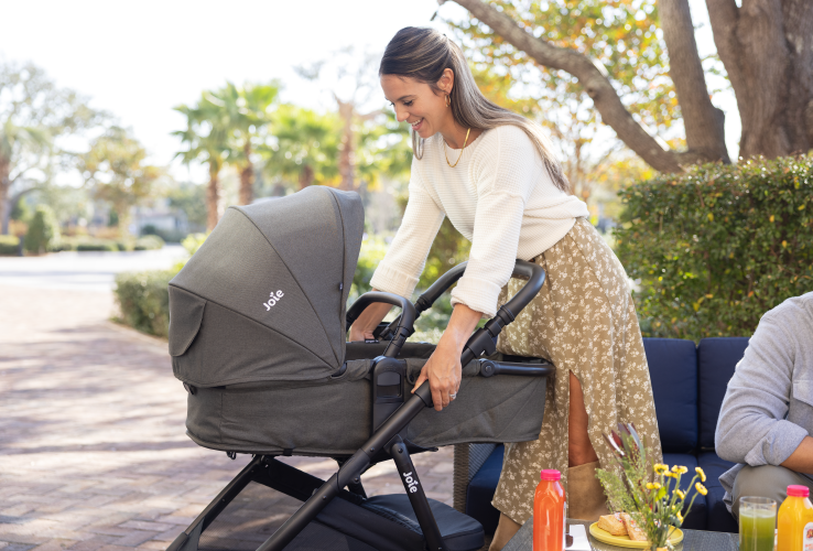 Mom smiling at ginger lx stroller in evergreen pramette mode adjusting stroller setting