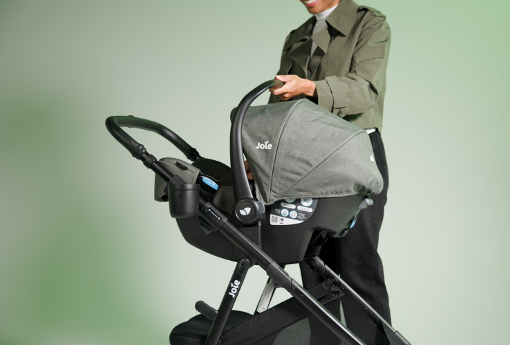 Mom using rue infant carseat in evergreen on ginger lx stroller as travel system on green background