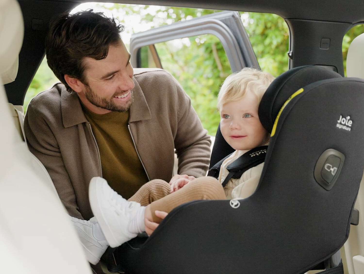 Young boy sitting rearward facing in the Joie Signature i-Prodigi Pro car seat while his dad smiles at him
