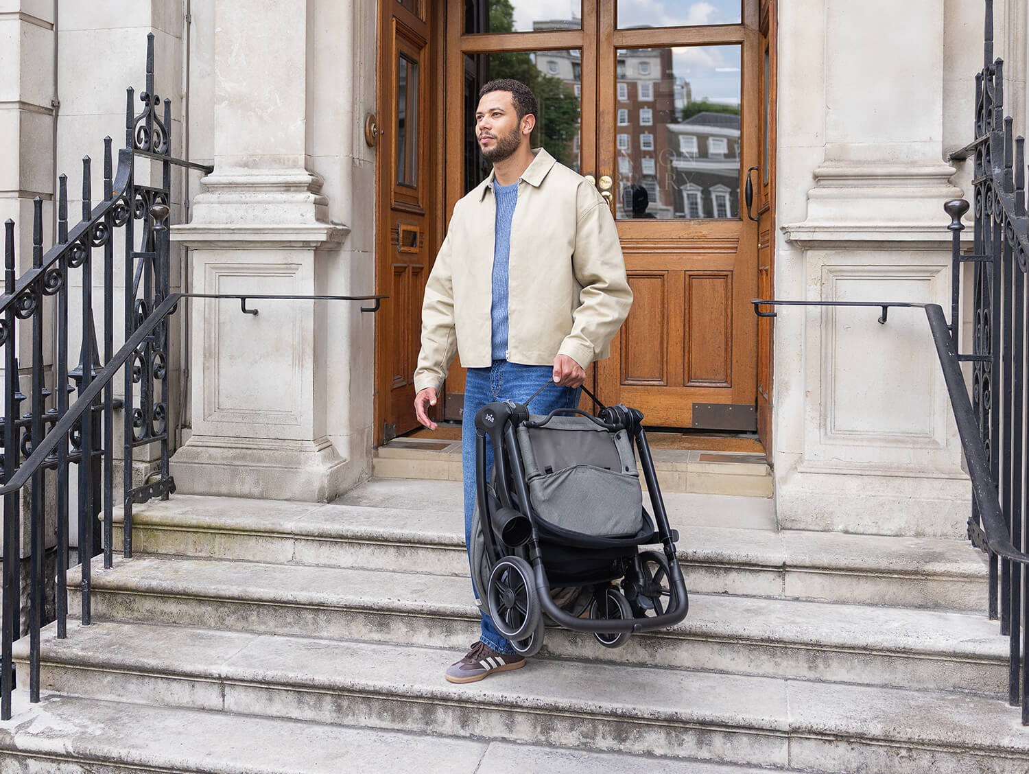 Dad walking down steps outside and carrying the folded Joie valora pram in one hand