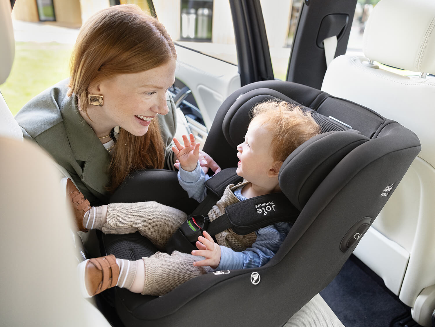 Little baby sitting rearward facing in the Joie Signature i-Prodigi Pro car seat and smiling and touching his mom