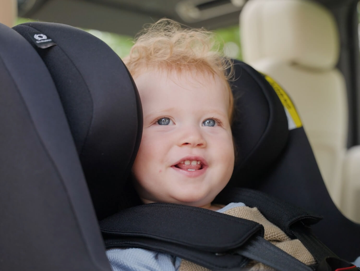 Little baby smiling with his head snug in the headrest of the Joie Signature i-Prodigi Pro car seat