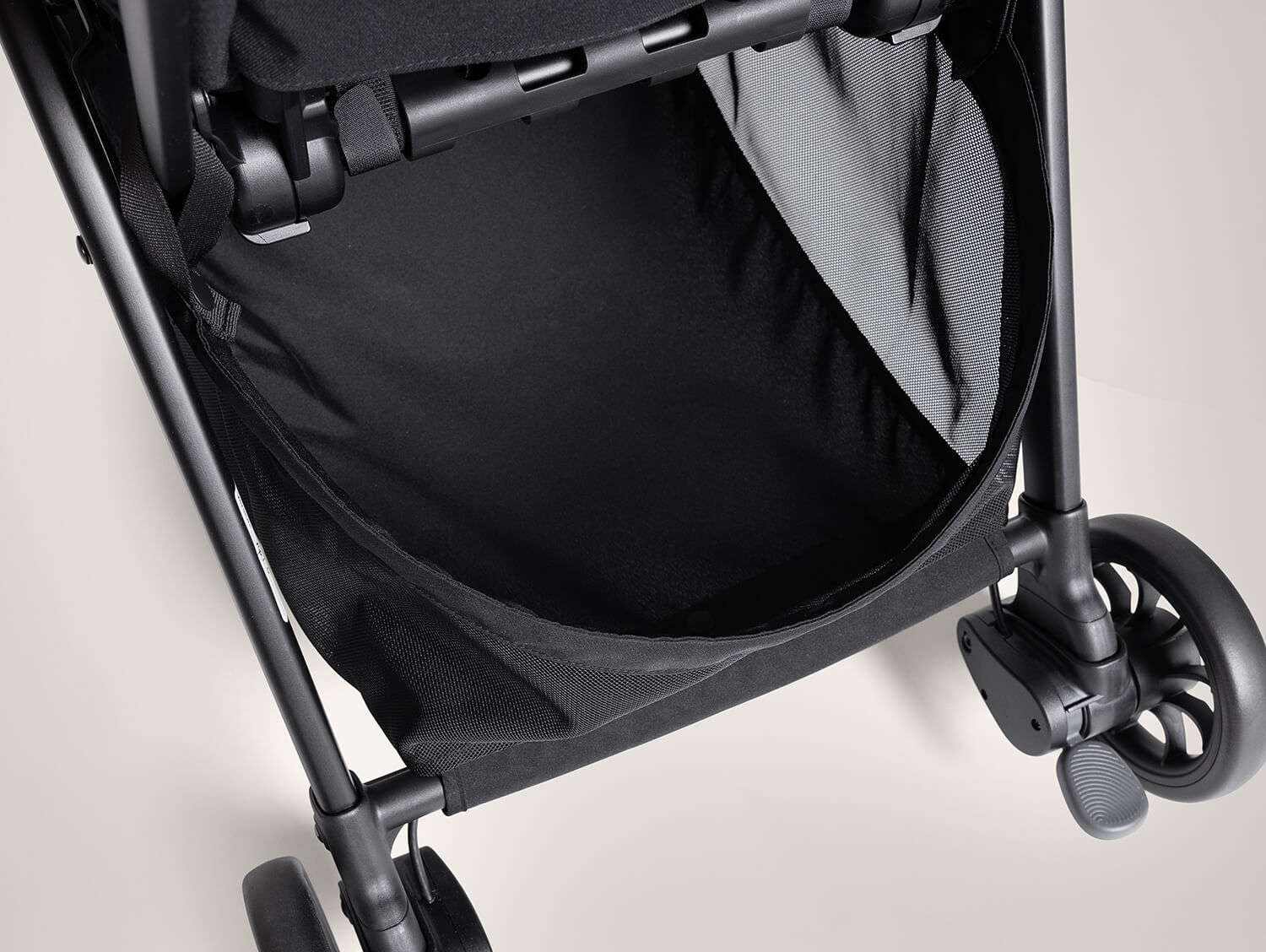 Large storage basket underneath the seat of the parcel pop travel stroller in eclipse black.
