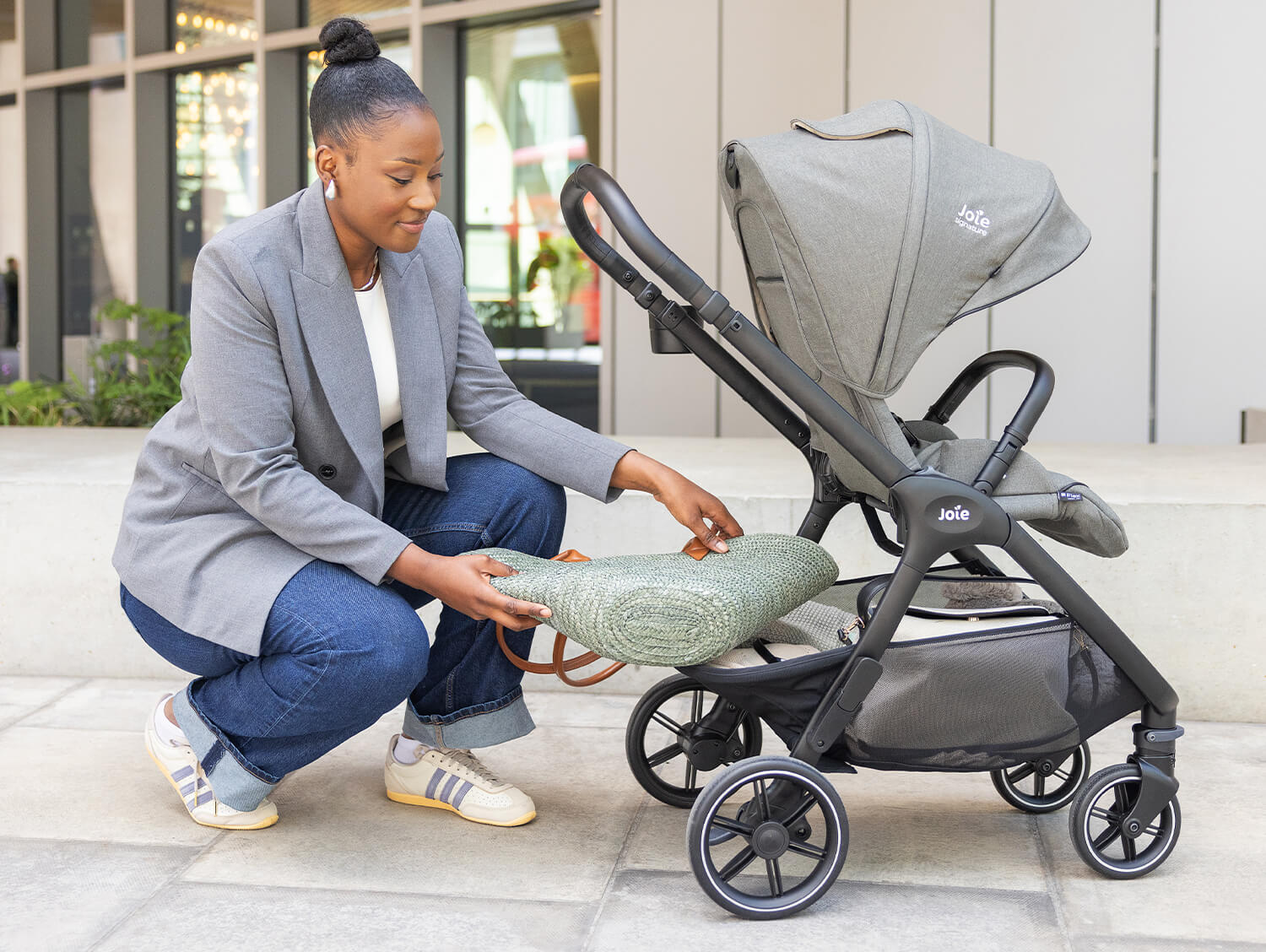 Mum outside bending down and putting her purse into the storage basket of the Joie valora pushchair