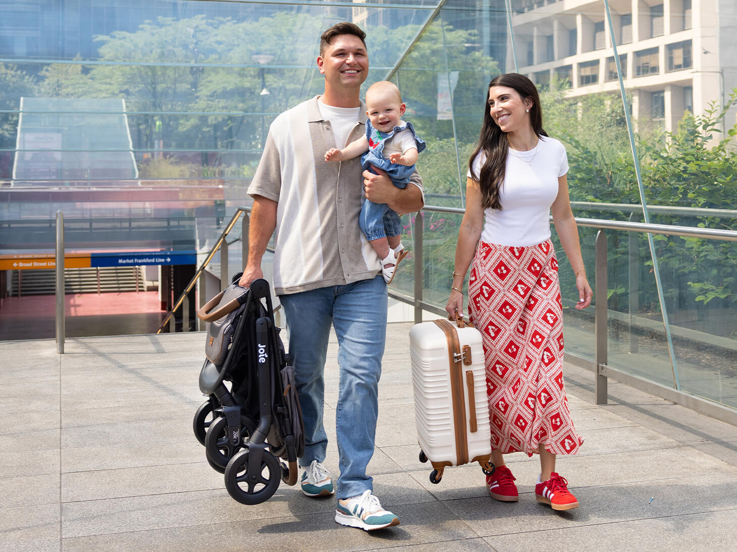Lifestyle photo of dad carrying Caraway Whirl easy fold stroller with swivel wheels and mom carrying luggage with wheels. 