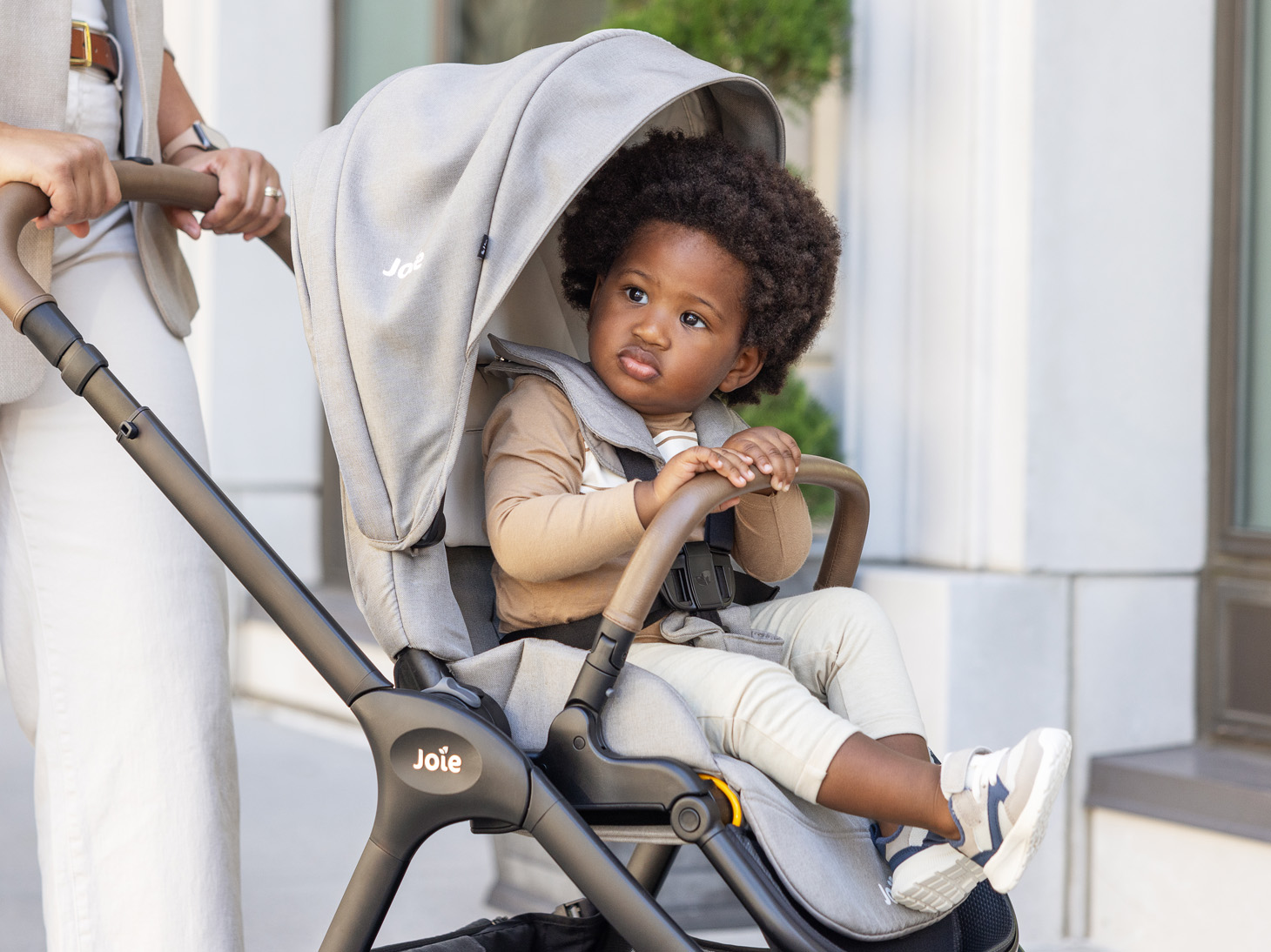 Mom pushing child secured in Kava stroller in dove