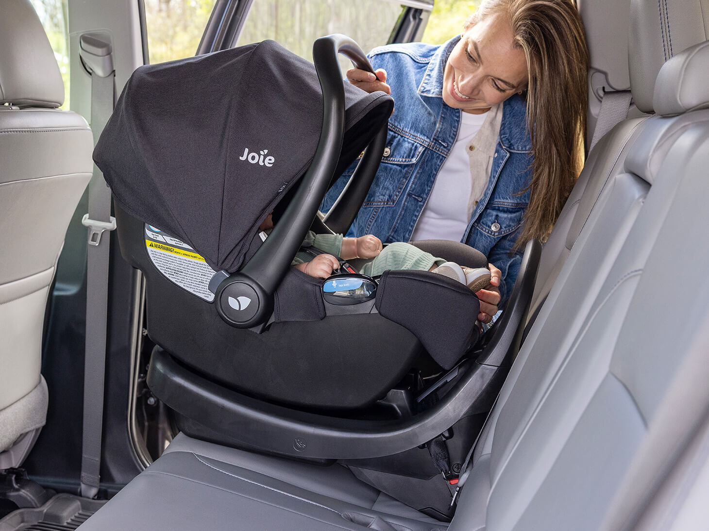 Mom with baby buckled in rue infant car seat secured on Base AR infant car seat base in black in car
