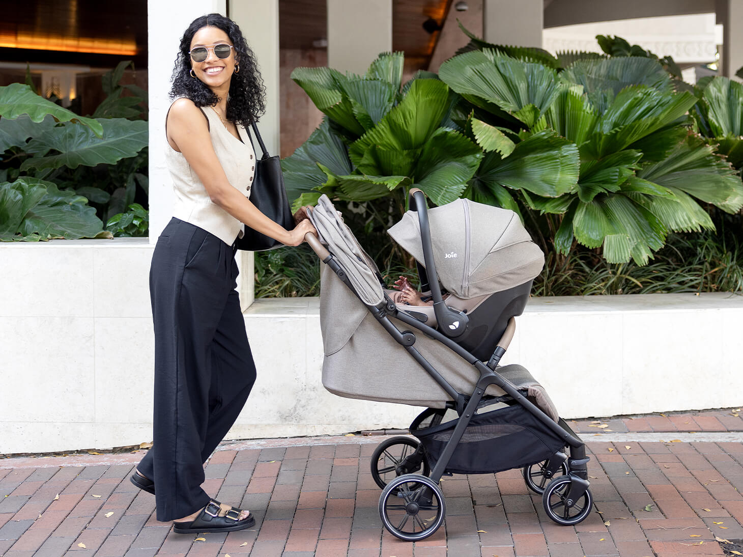Parent strolling with nutmeg and mint latch travel system on sidewalk
