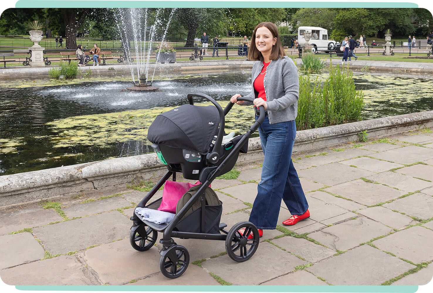 Mum in a park strolling with the Joie chrome 2 pram with an infant car seat attached to the frame of the pram