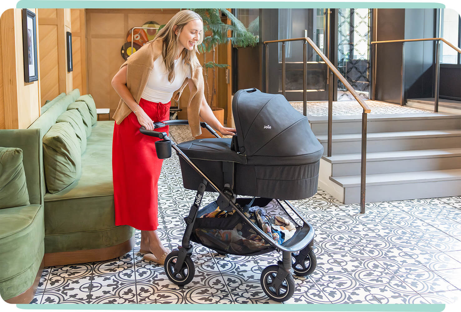 mum checking in on baby in the Joie versadrift pram with carry cot attached in a hotel lobby