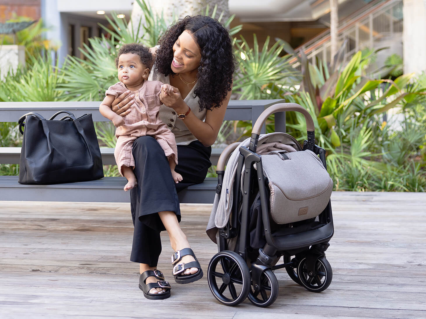 Nutmeg stroller folded next to parent and baby on bench
