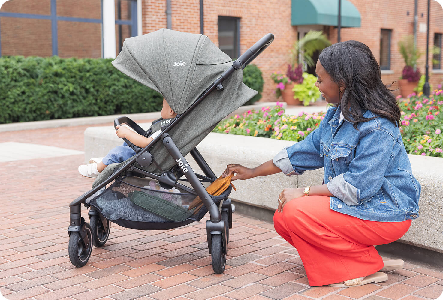mum outside on the sidewalk bending down and putting a bag in the large storage basket of the joie mydrift travel stroller