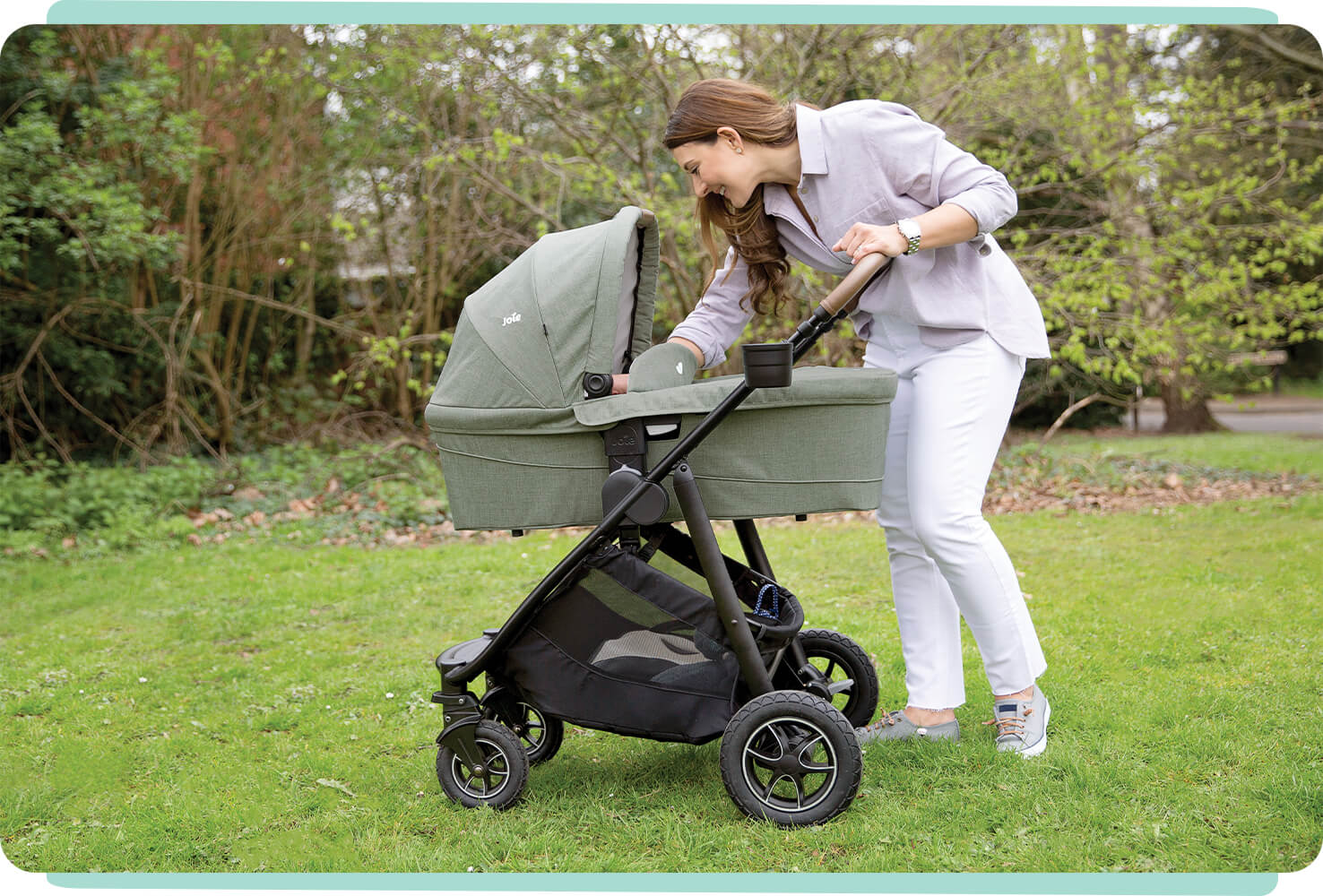  Joie Ramble xl carry cot in light green sitting on pushchair with women leaning over push bar reaching for baby in carry cot. 