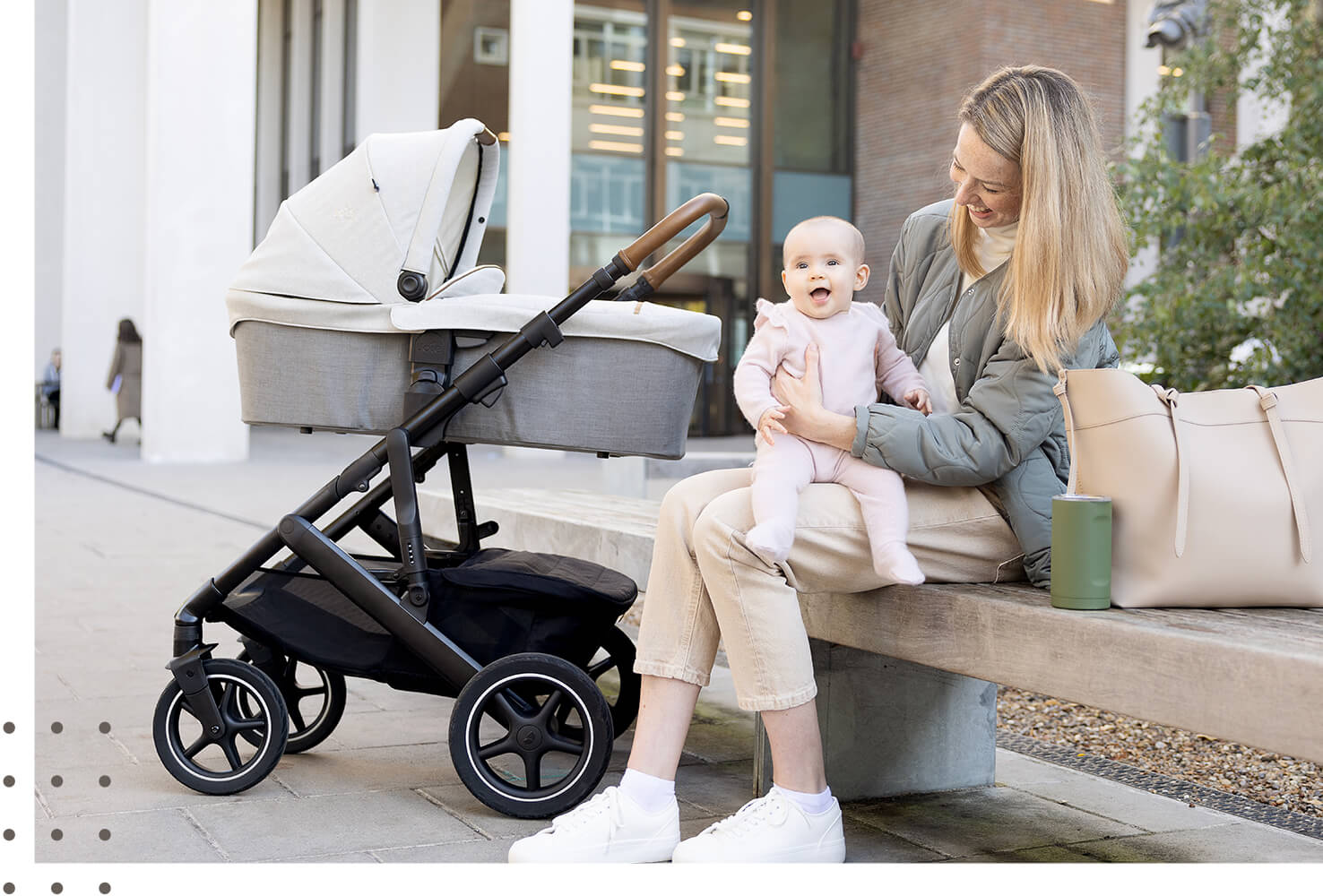 Mom and baby sitting on bench with ramble XL carry cot in gray on vinca’s frame