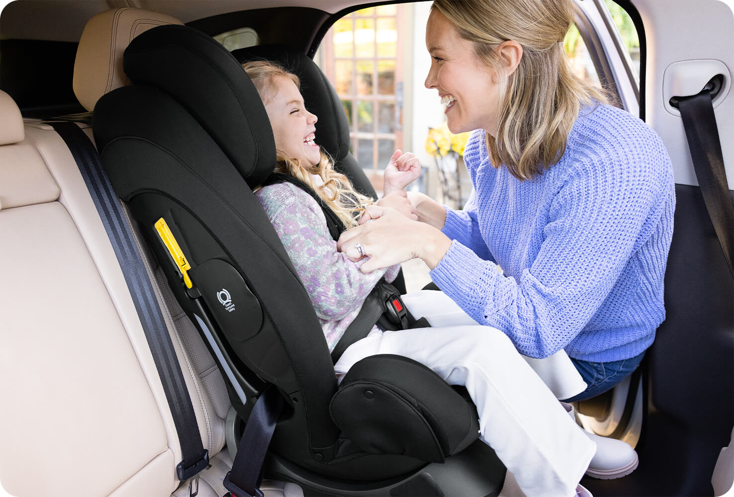 An image of a mother adjusting the harness of the Joie Centra car seat with her daughter smiling in the seat. 