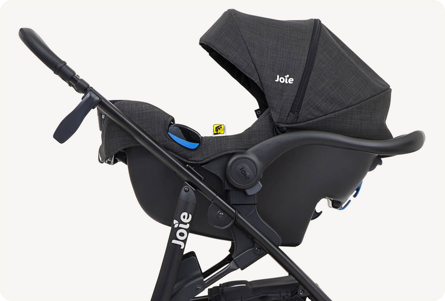   Joie mytrax stroller in black with infant carrier attached, zoomed in to show where it attaches to the stroller base. 