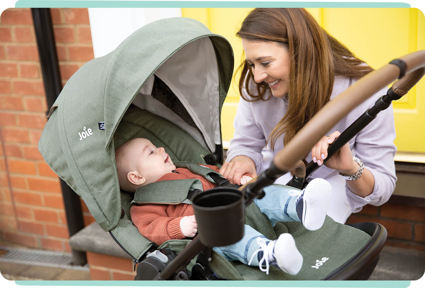  Mom smiling at baby who is sitting in light green Joie versatrax pram.