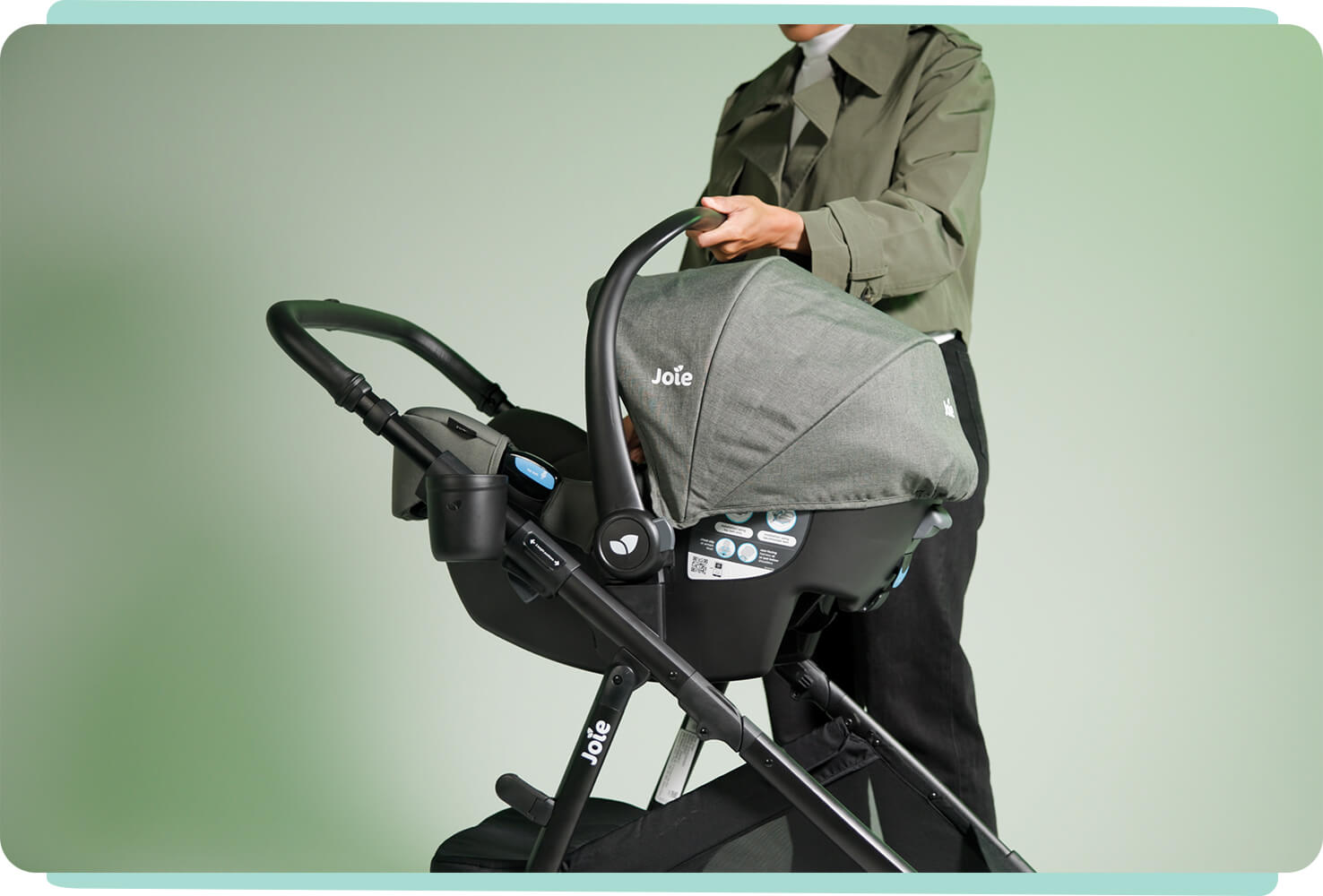 A mother smiles as she demonstrates attaching an infant car seat to the Joie ginger lx in green
