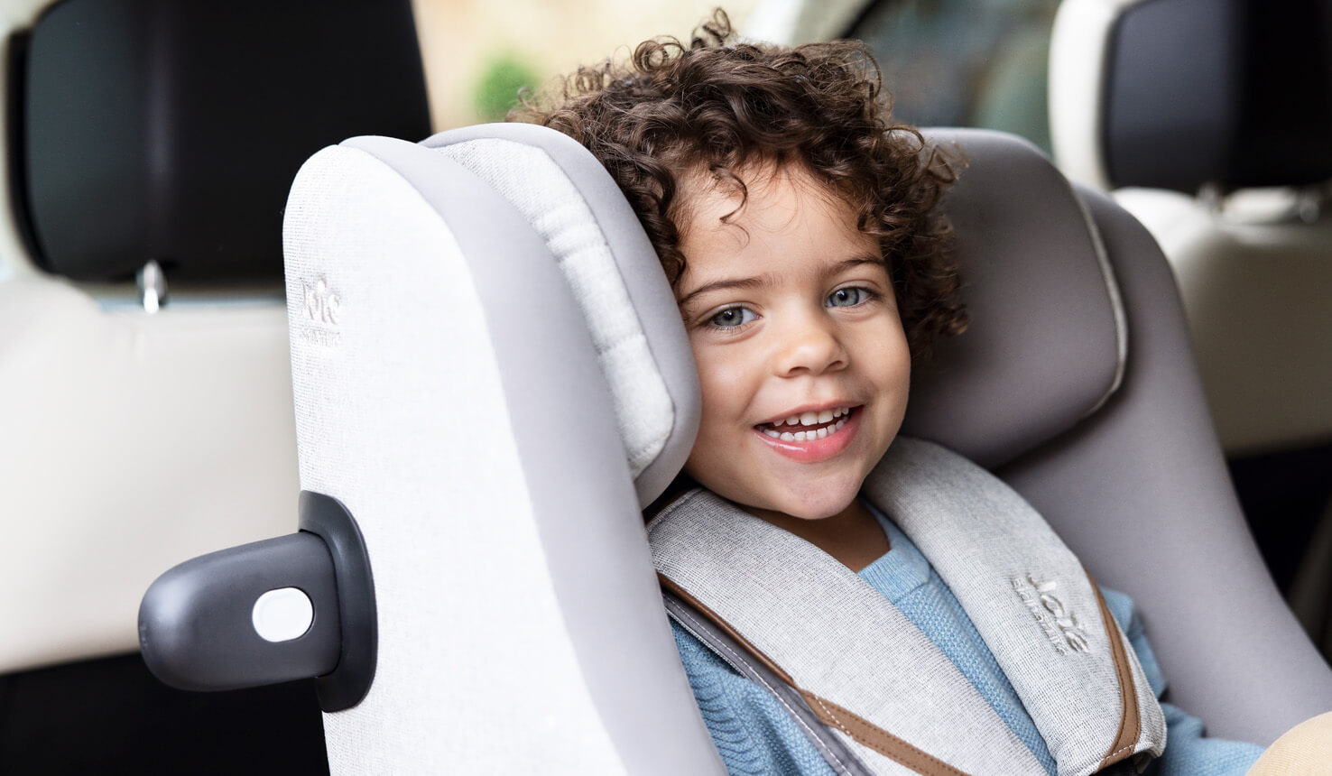 Nahaufnahme eines kleinen Jungen, der in einem grauen Joie i-Harbour Kindersitz lächelt.