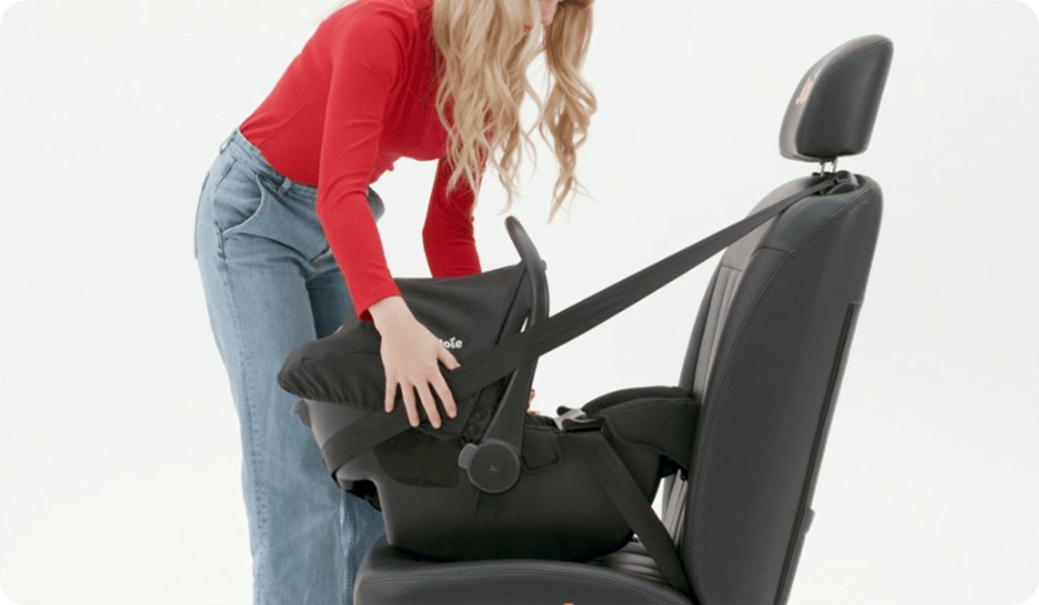 Frau installiert    Joie i-Juva Babyschale auf einem Sitz mit Sicherheitsgurt.