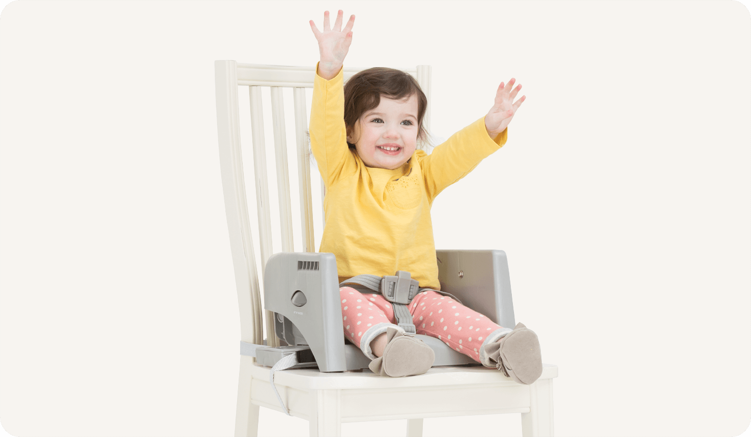 Kind sitzt auf einer grauen Sitzerhöhung, die Teil des Mulitply Hochstuhls auf einem weißen Stuhl ist. 