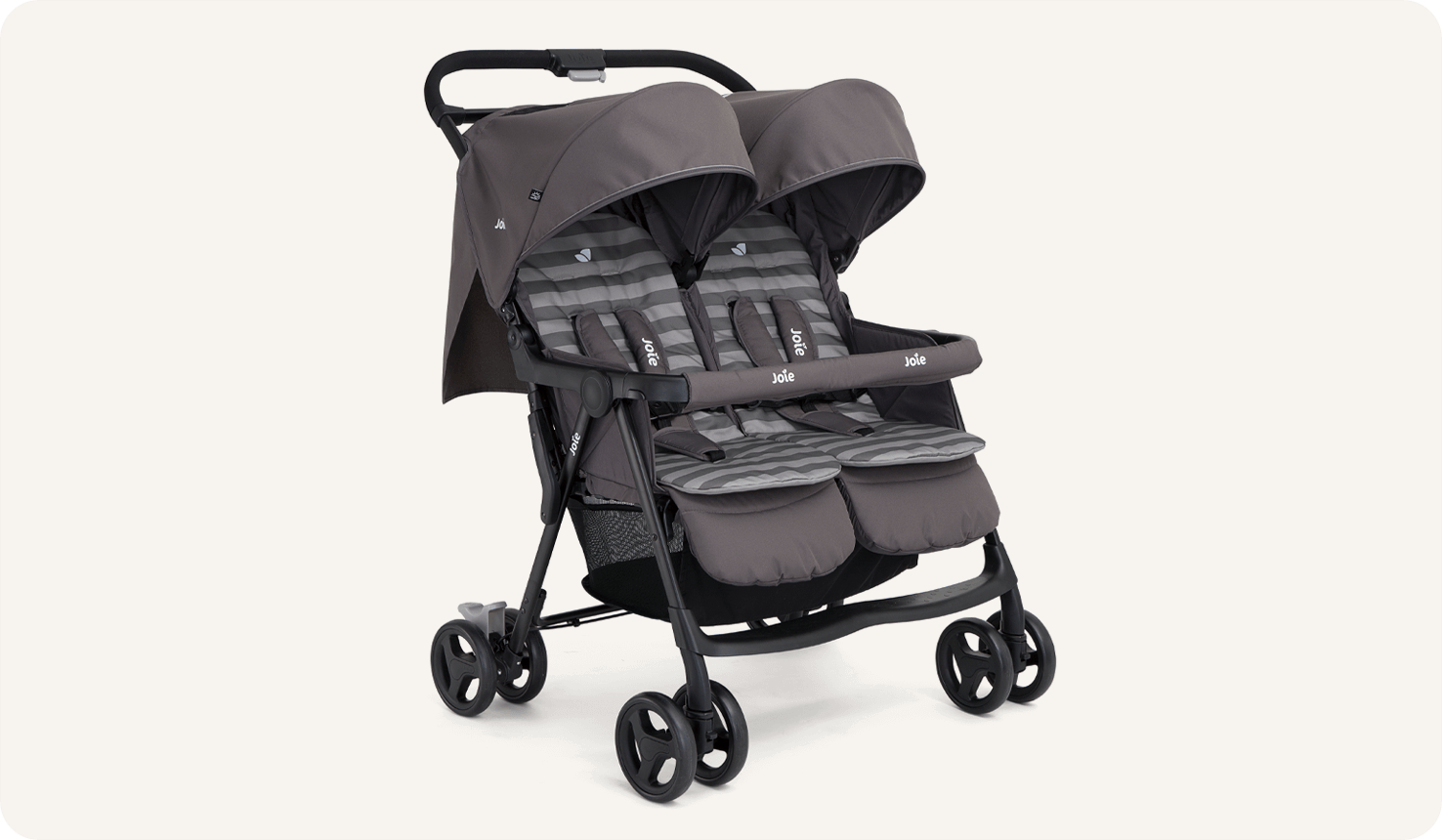  The Joie Aire Twin side-by-side double stroller in dark gray at an angle, with a peach coloured seat insert on the left seat and a light blue insert on the right seat.