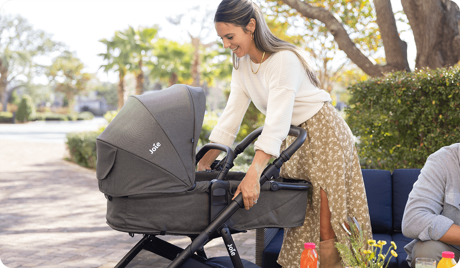 A mother smiles in a park setting as she adjusts the height of the pramette on the Joie ginger lx in green.
