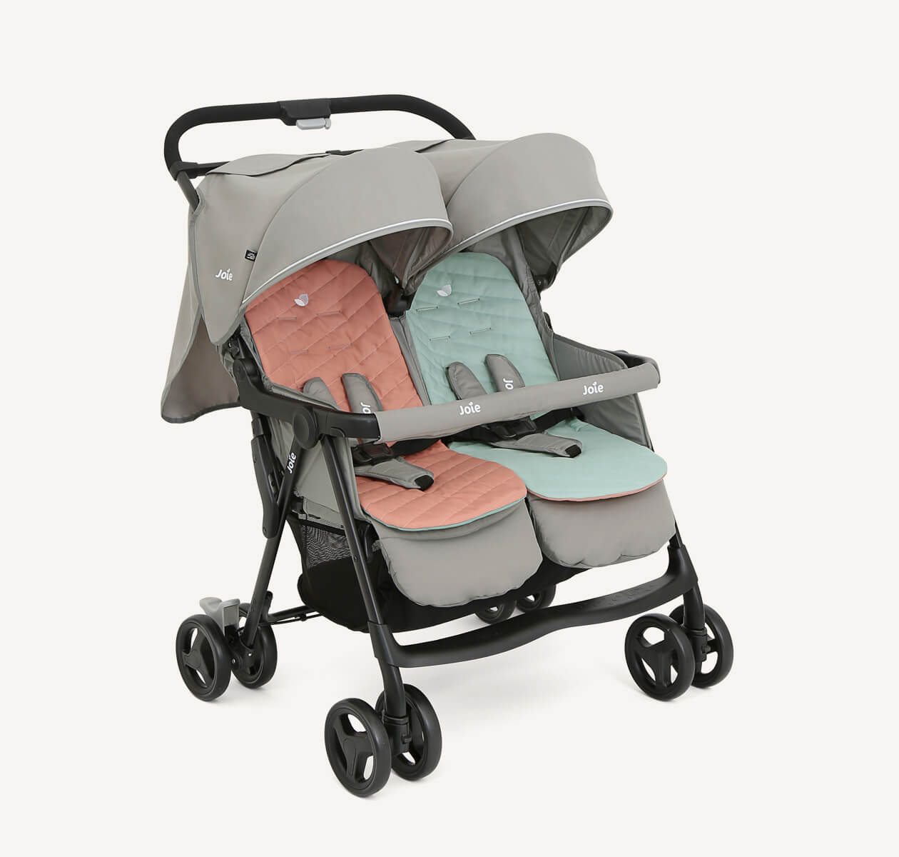  The Joie Aire Twin side-by-side double stroller in light gray at an angle, with a peach coloured seat insert on the left seat and a light blue insert on the right seat.