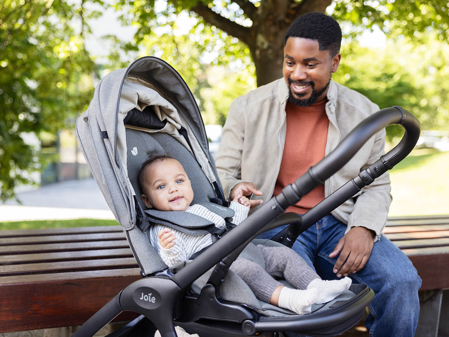 Dad interacts with his baby in a Joie Signature finiti pram while sitting on a park bench.