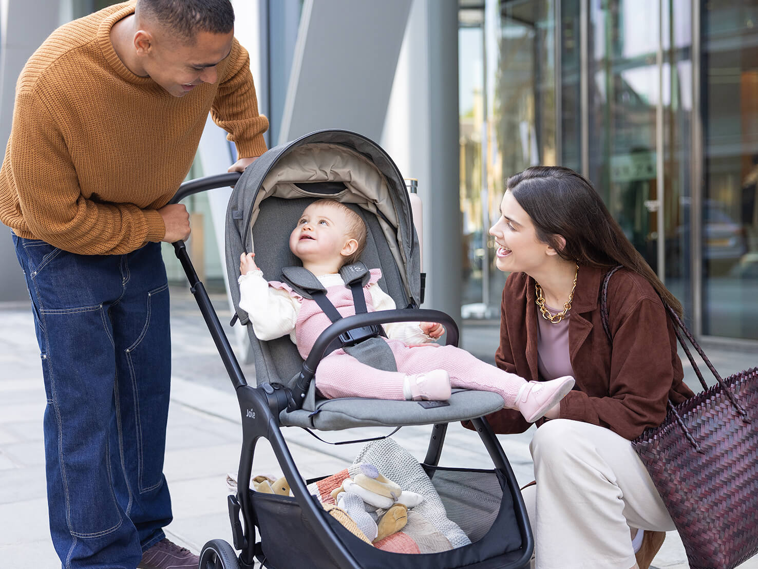 Mother and father smiling at baby in Joie Signature valora pushchair in grey.
