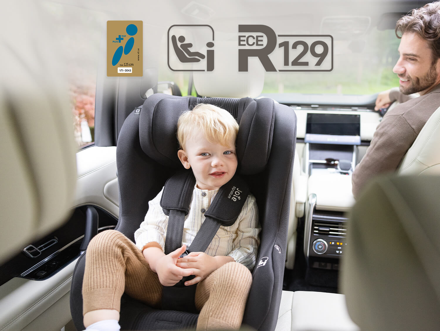 Young boy sitting rearward facing in the Joie Signature i-Prodigi Pro car seat while his dad is smiling back at him from the front seat with Swedish Plus Test, i-Size and R129 logos