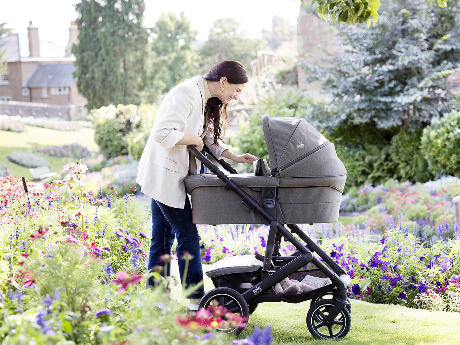 Mom cooing at baby in a Joie Signature pram while walking through a botanical garden. 
