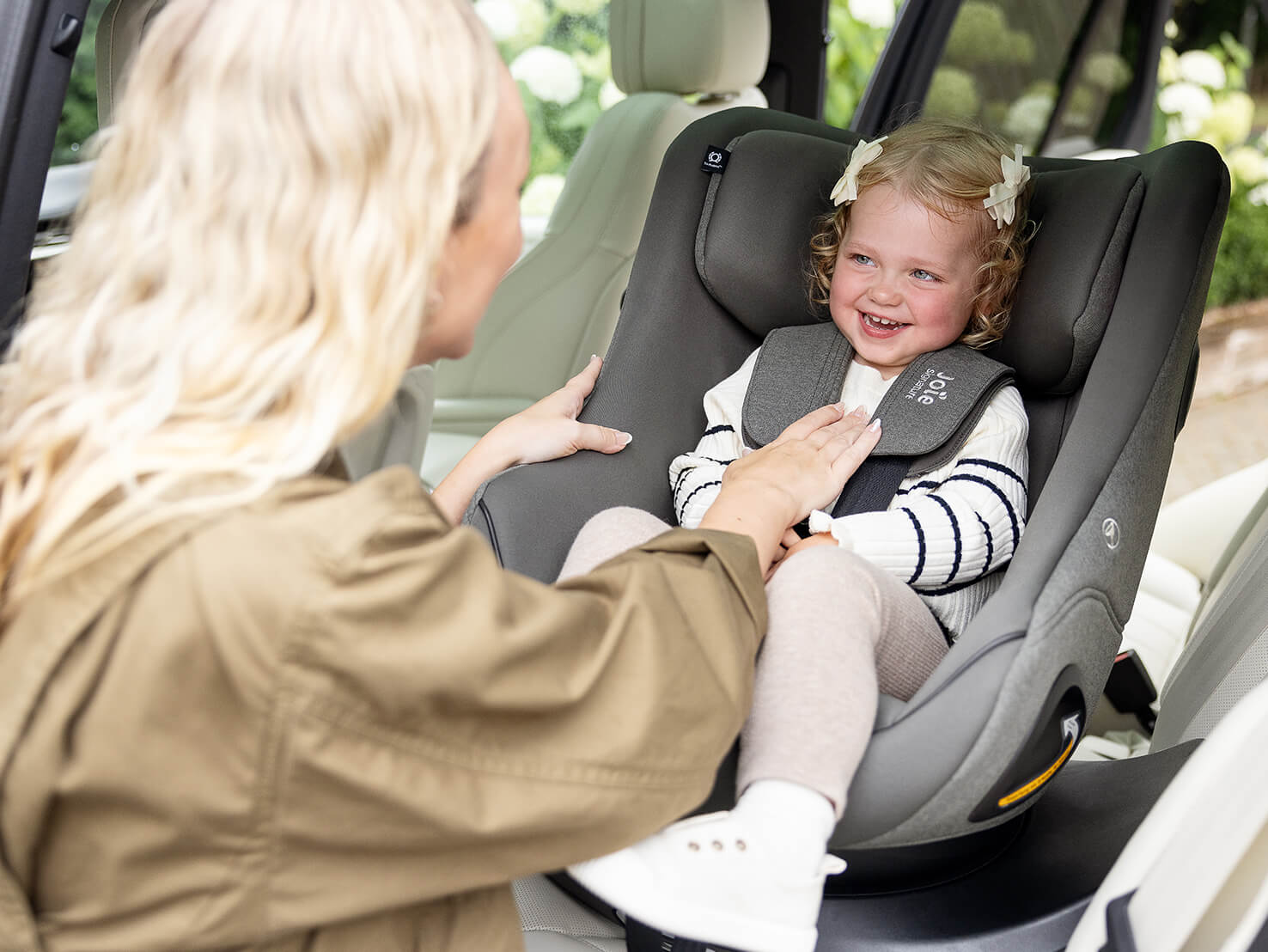 Mother loading toddler into Joie Signature i-Harbour E car seat in grey, installed using i-Base Encore spinning car seat base.
