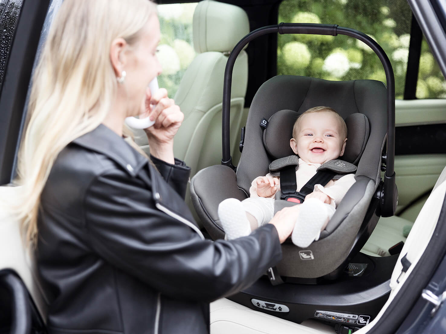 Mother loading baby into Joie Signature car seat i-Level Pro in grey into the car, installed in the car using spinning car seat base i-Base Encore in black.
