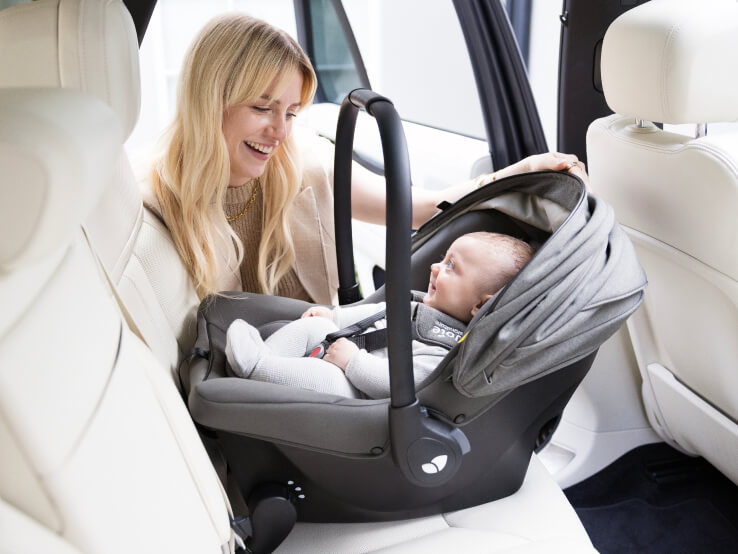 Mother loading infant into Joie Signature sprint infant car seat in grey, showing the integrated ISOFIX connectors installed into the car.

