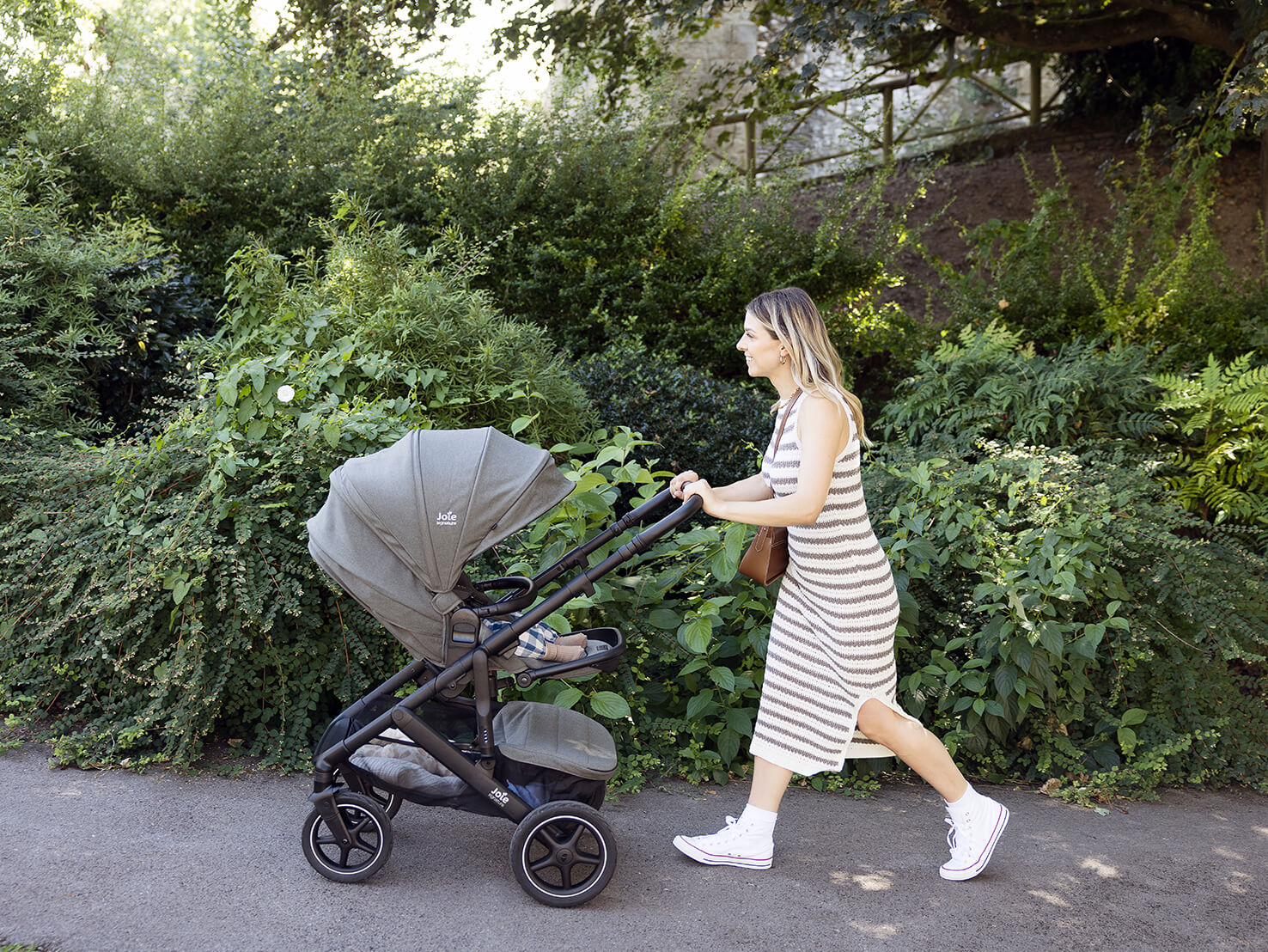 Mom pushing toddler on a nature path in a Joie Signature vinca pram.
