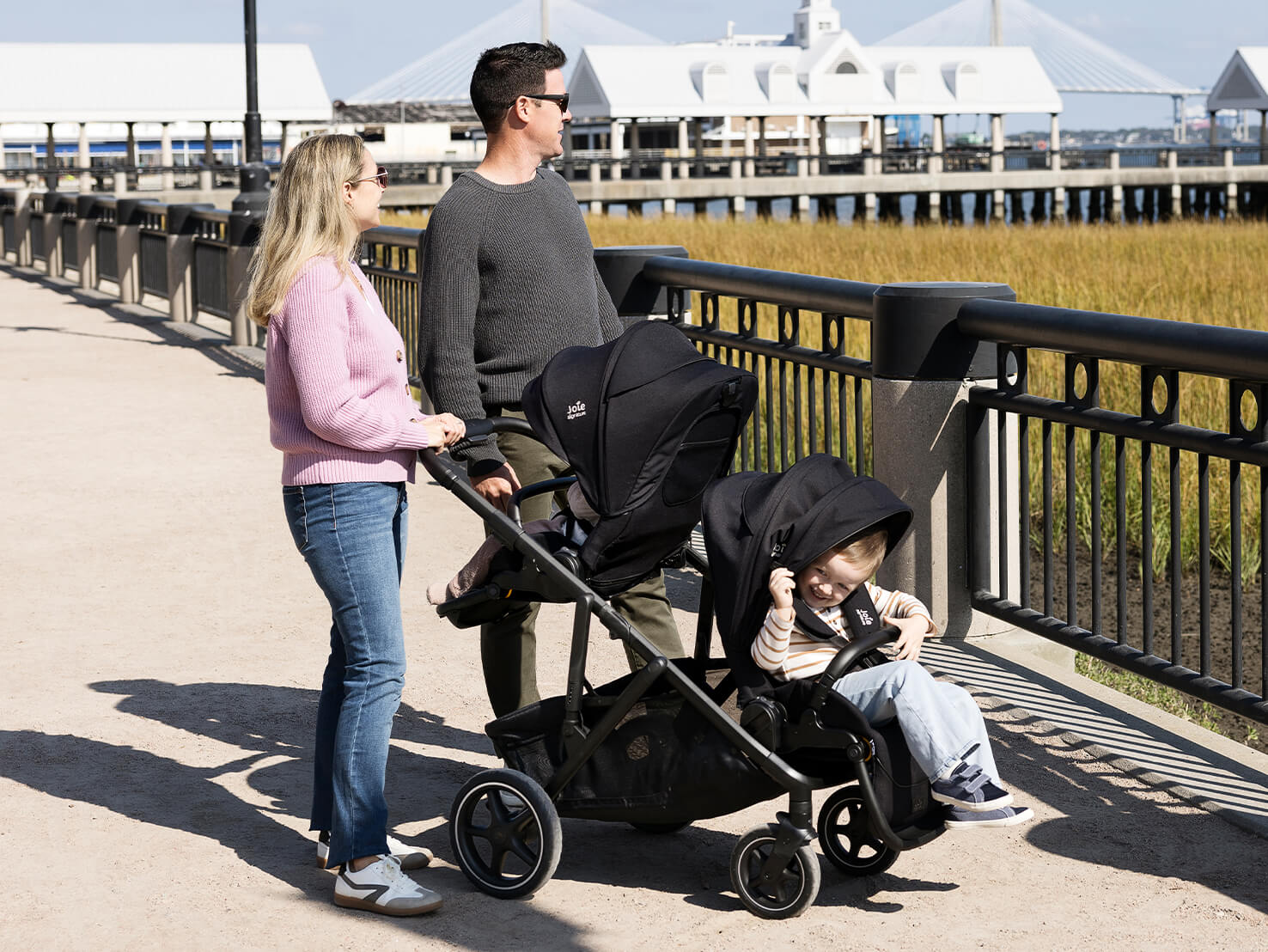 Mother and father walking with two children in Joie Signature versiti pushchair in black, one seat is world facing and the second seat is parent facing.