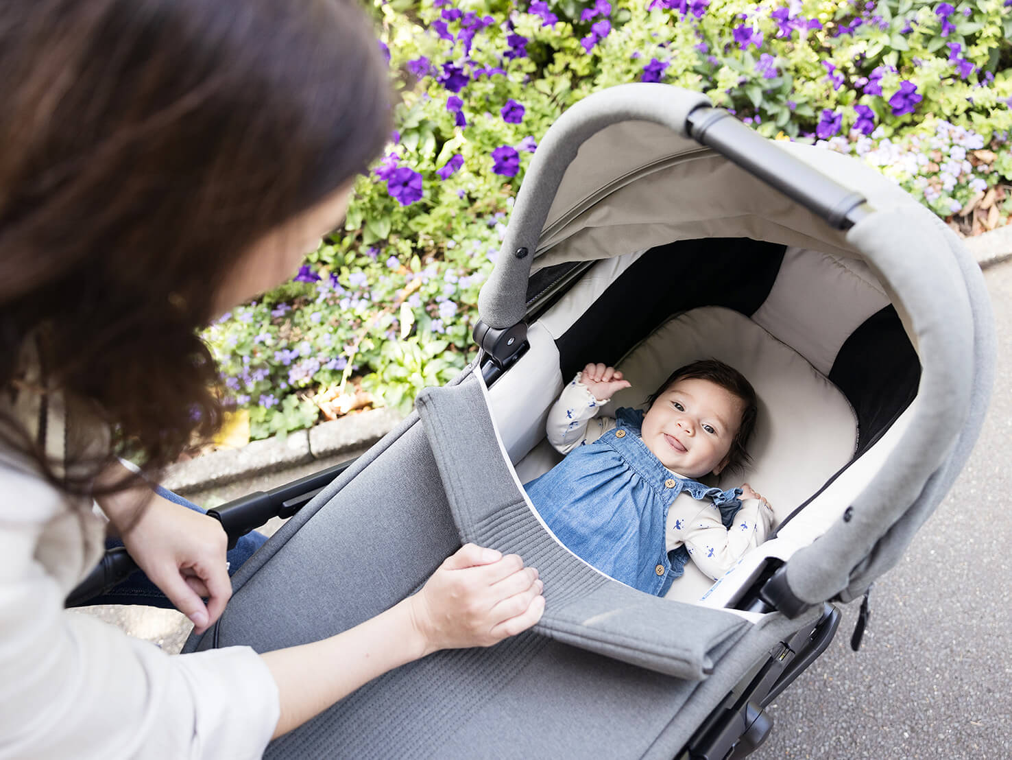 Mother looking into Joie Signature ramble xl carry cot in grey to see baby laying comfortably and happily on plush padded fabrics.

