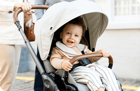 Lächelndes Kleinkind in einem Joie finiti Signature Kinderwagen in Hellgrau.