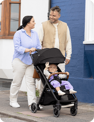 Parents marchant avec un bébé joyeux installé dans un Joie pact pro, coloris noir. 