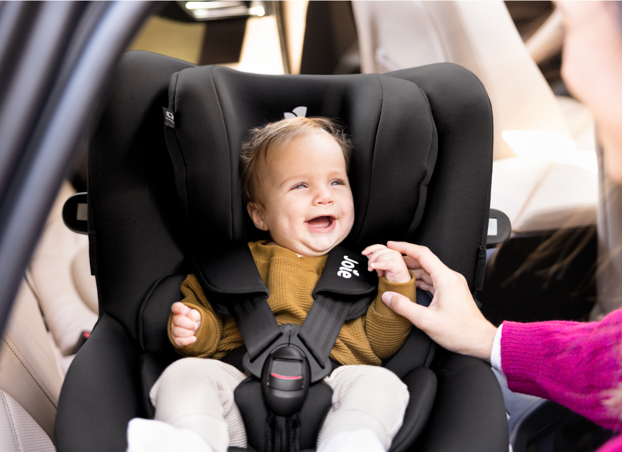 smiling baby installed in a black Joie i-spin 360 car seat. 