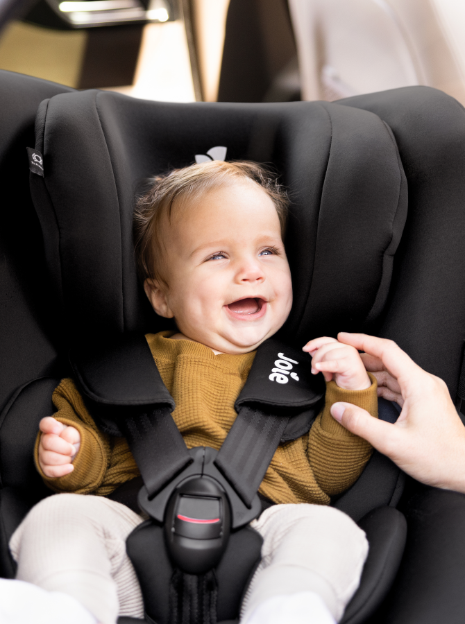 smiling baby installed in a black Joie i-spin 360 car seat. 