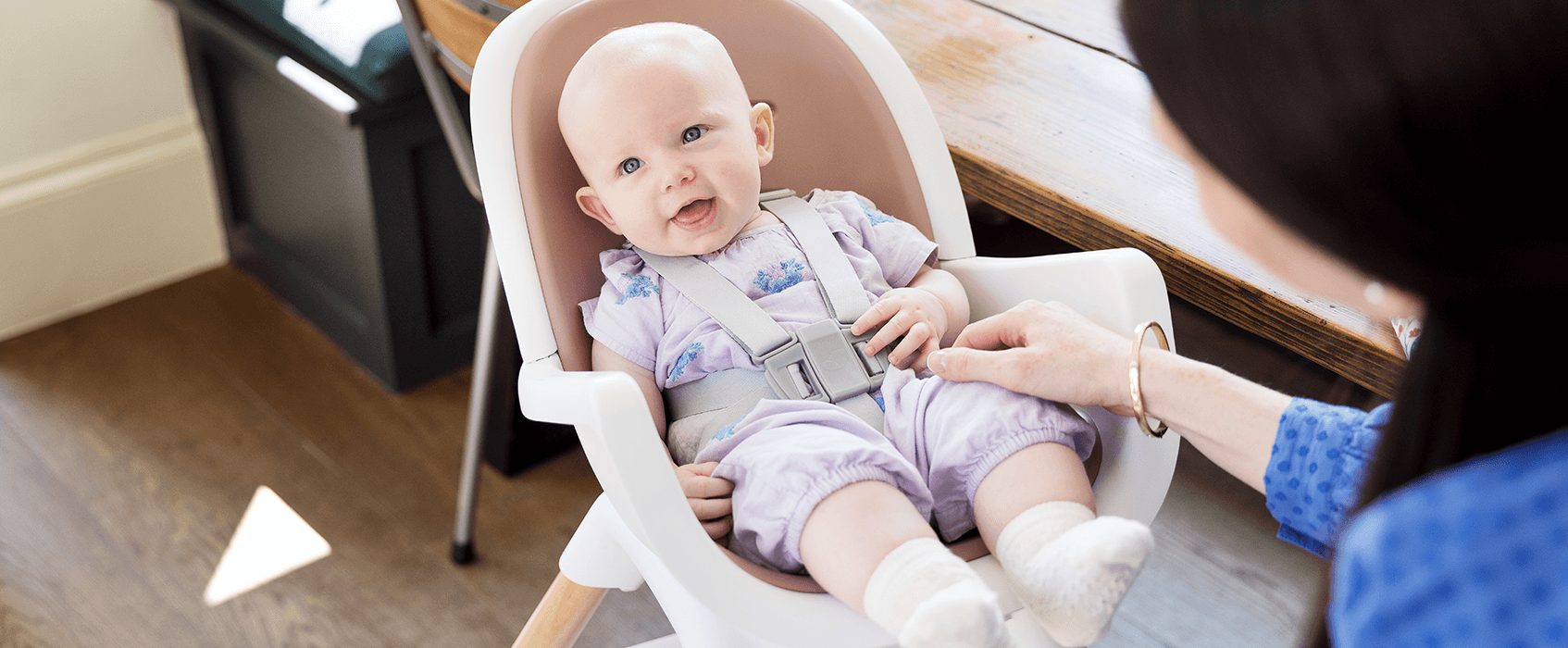 Baby sitting in a brown and white Joie chestnut highchair, looking to the left.