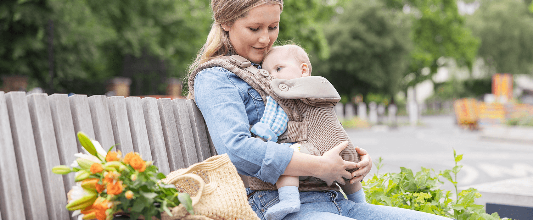 Mum cuddling baby in a mustard yellow Joie Savvy air baby carrier