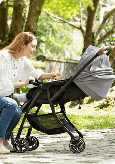 Image of a mother sitting down and looking at baby in a stroller.