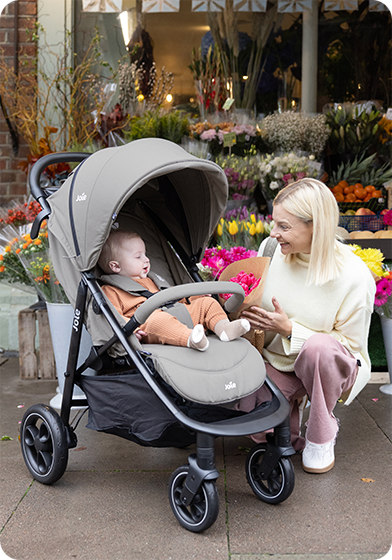 Mother kneels beside baby sitting comfortably in gray Joie Litetrax pushchair.