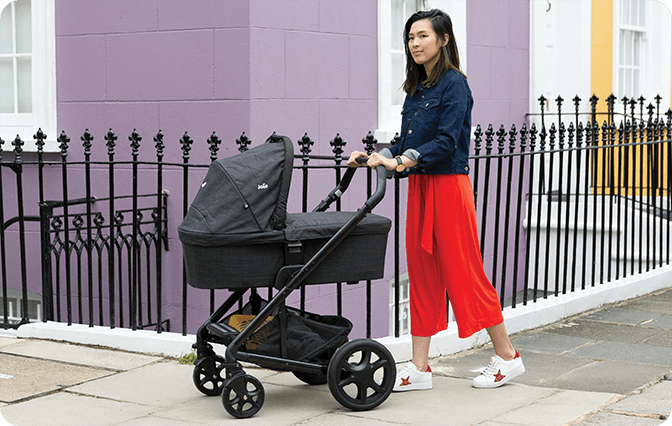 Image of a mum pushing the Joie chrome DLX stroller with the matching carry cot attached.