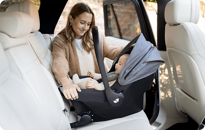 Madre contenta colocando a su bebé en el portabebés Sprint en el asiento trasero del coche