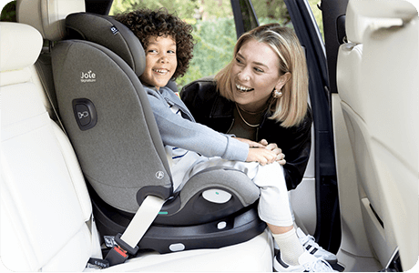 Happy child in gray Joie i-Spin XL car seat as parent interacts from outside the car.