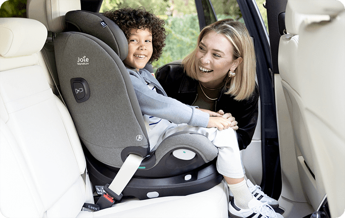 Happy child in gray Joie i-Spin XL car seat as parent interacts from outside the car.